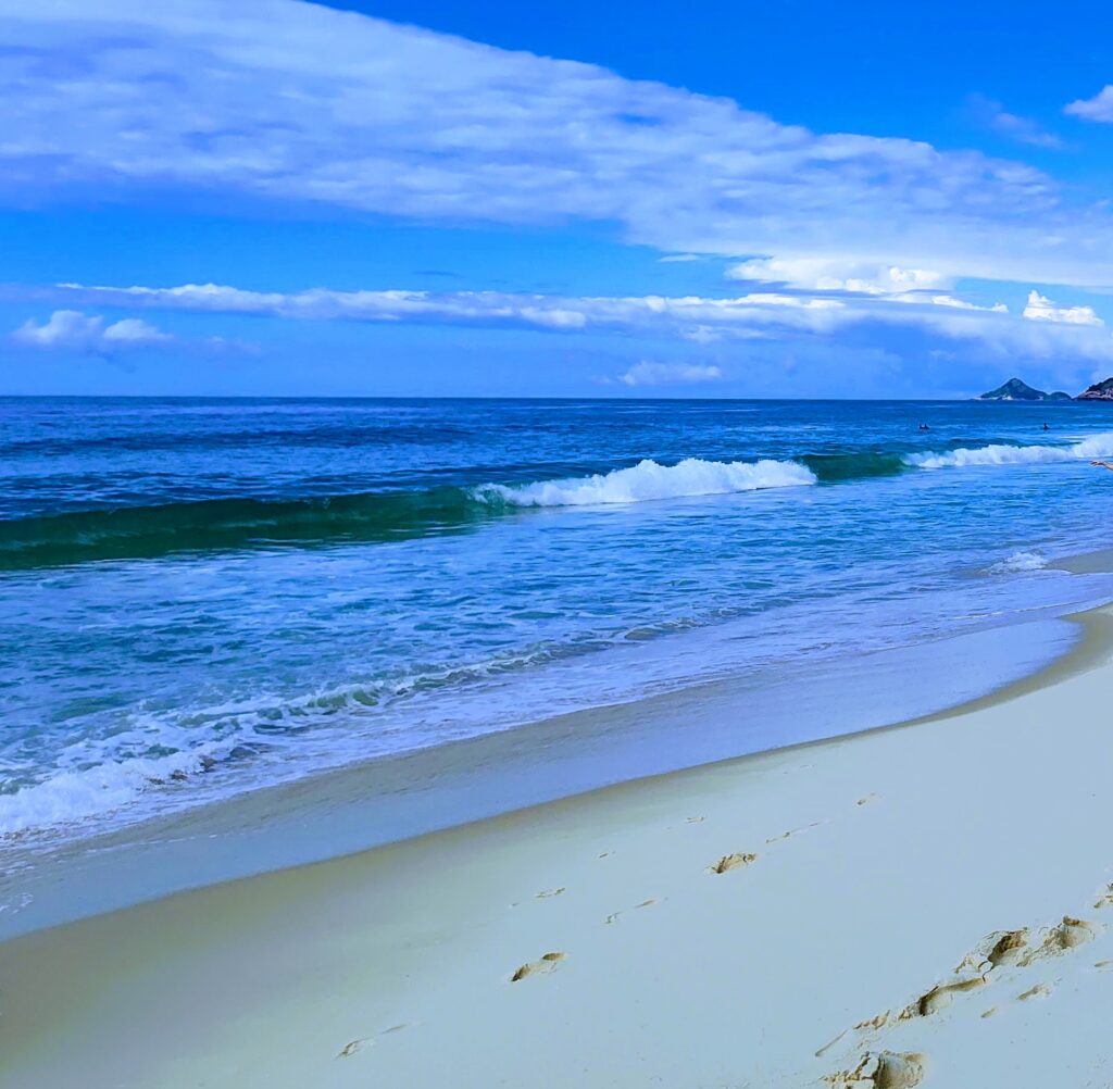 Foto de uma praia, com as ondas e a faixa de areia mais próxima ao mar.